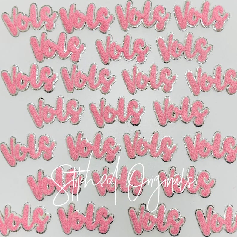 May include: A collection of pink felt iron-on patches with the word "Vols" in a cursive font. The patches have a silver outline.