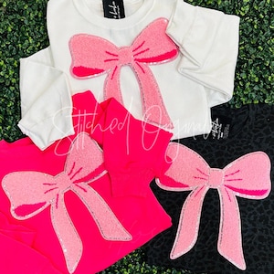 May include: Three shirts with pink fuzzy bow appliques. The shirts are white, hot pink, and black with a leopard print.