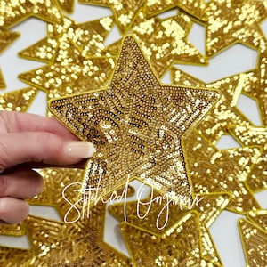 May include: A close-up of a gold sequined star-shaped patch. The patch is surrounded by other gold sequined star-shaped patches.