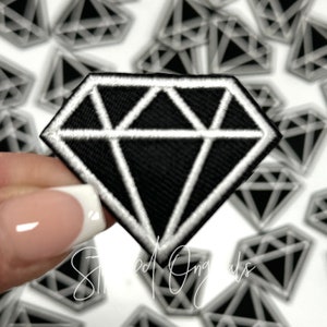 May include: A black diamond-shaped patch with a white outline. The patch is made of fabric and has a stitched design.