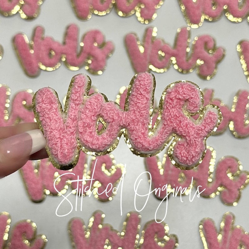 May include: Pink fluffy fabric patches with gold glitter trim spelling out the word "YOLO".