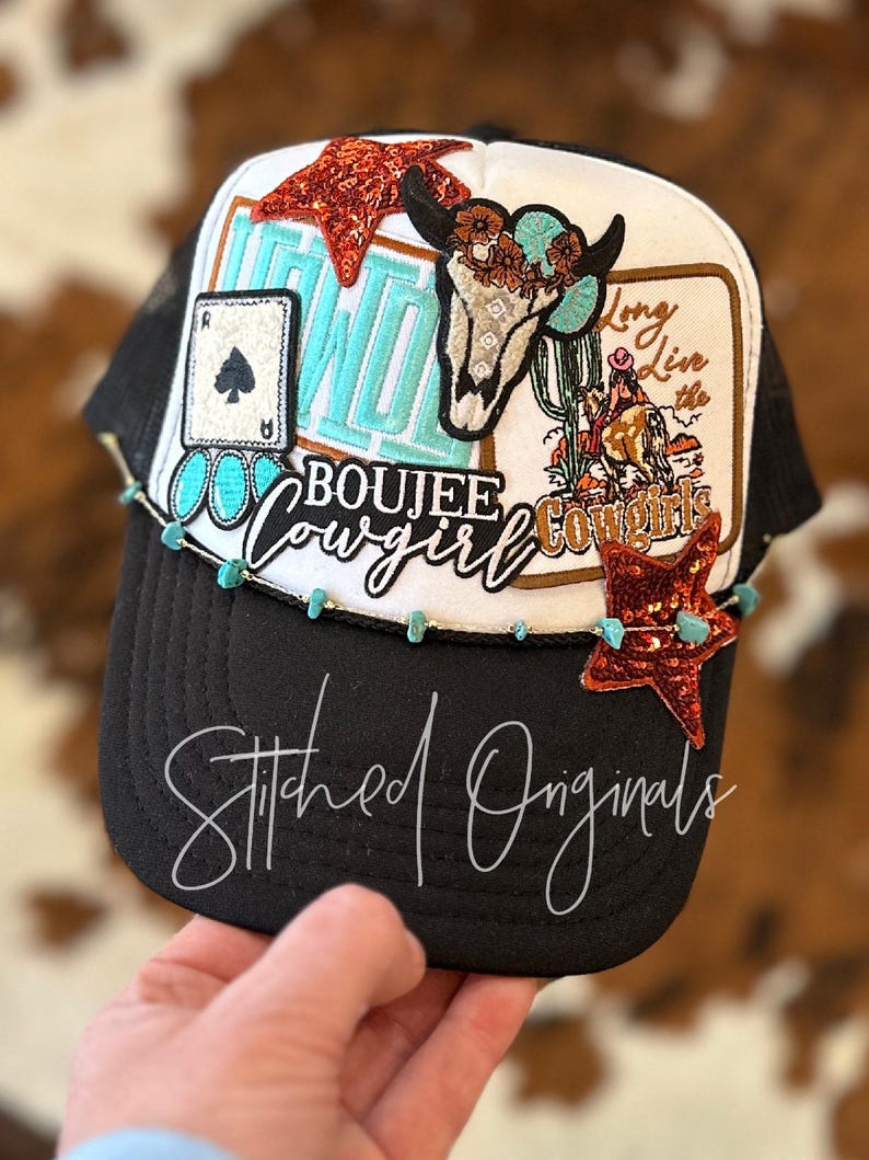 May include: Black and white trucker hat with a variety of colorful patches, including a turquoise skull with a floral crown, a turquoise and orange star, a turquoise and white patch that says "Long Live the Cowgirls", and a turquoise and white patch that says "Boujee Cowgirl".