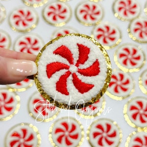 May include: Embroidered peppermint candy patch with a white center and red swirl design, surrounded by gold glitter. The patch is held up in front of a background of similar patches. The text "Stitched Originals" is visible.