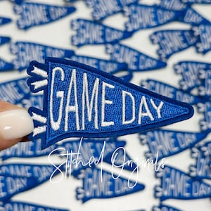 May include: A blue felt pennant with white embroidery that reads "GAME DAY". The pennant is a popular item for sports fans and tailgating.
