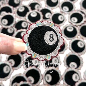 May include: Embroidered patch featuring a black eight ball with a white number 8. The patch has a decorative scalloped edge with teal and orange accents, and a burgundy border. The text "Stitched Original" is written in cursive.
