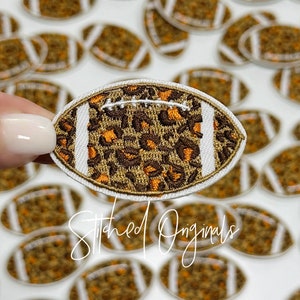May include: A brown and orange leopard print football patch with white stitching. The patch is surrounded by other football patches.