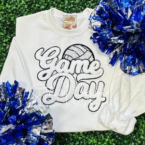 May include: White sweatshirt with a black and white graphic of a volleyball and the text "Game Day".