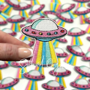 May include: A collection of colorful embroidered iron-on patches featuring a pink and white UFO with rainbow stripes. The patches are perfect for adding a fun and quirky touch to clothing, bags, or other accessories.