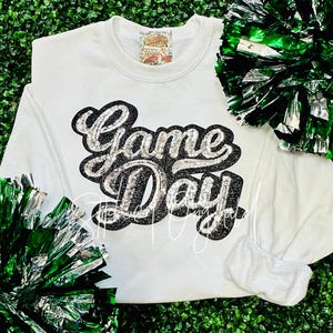 May include: White sweatshirt with a black and silver glitter design that says "Game Day".