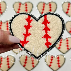 May include: A white heart-shaped patch with a red baseball design. The patch has a silver glitter trim.
