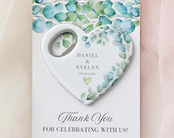 May include: A heart-shaped bottle opener featuring a watercolor eucalyptus leaf design. The text reads DANIEL & EVELYN 06.08.2025. It is attached to a white card with the text Thank You FOR CELEBRATING WITH US! and matching green foliage.