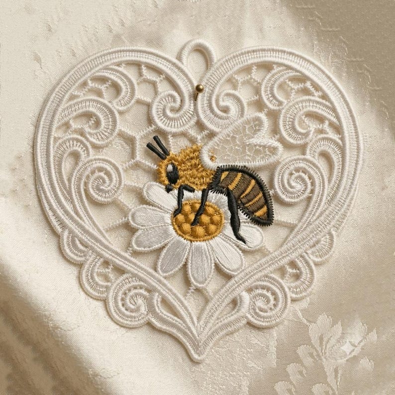 Puede incluir: Aplique de encaje blanco en forma de coraz&oacute;n con un dise&ntilde;o detallado. Una abeja bordada en amarillo, negro y marr&oacute;n est&aacute; posada sobre una margarita blanca con un centro amarillo. El aplique tiene un peque&ntilde;o lazo en la parte superior para colgar.