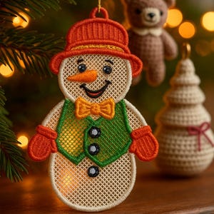 May include: Embroidered snowman Christmas ornament with an orange hat, carrot nose, and green vest. The snowman has a yellow bow tie and black buttons. Other ornaments include a crocheted bear and Christmas tree.