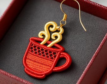 Puede incluir: Un solo pendiente de taza de café roja bordada con detalles de vapor dorados. El pendiente está colocado sobre un fondo gris oscuro dentro de una caja de joyería roja. El pendiente tiene un gancho dorado.