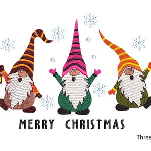 Könnte beinhalten: Gesticktes Design mit drei Weihnachtszwergen mit weißen Bärten und bunten Hüten. Ein Zwerg hält eine Laterne, umgeben von Schneeflocken. Der Text "MERRY CHRISTMAS" steht darunter, mit "Three Sizes" darunter.