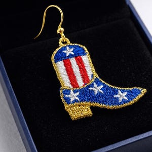 May include: Embroidered earring in the shape of a cowboy boot, featuring a blue background with white stars and a red and white striped design. The boot has a gold-colored heel and trim, and a gold-colored hook.