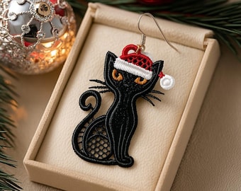 May include: A black cat-shaped earring with a Santa hat, displayed in a beige box. The earring is made of black lace with orange eyes and whiskers. A silver-colored earring hook is attached. Christmas ornaments and greenery are in the background.