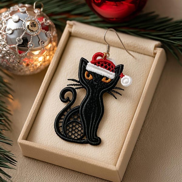May include: A black cat-shaped earring with a Santa hat, displayed in a beige box. The earring is made of black lace with orange eyes and whiskers. A silver-colored earring hook is attached. Christmas ornaments and greenery are in the background.