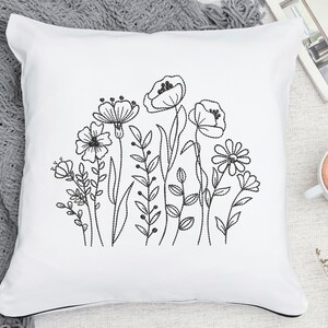 Op de afbeelding: Een wit kussen met een zwart geborduurd bloemenmotief met verschillende bloemen en bladeren.