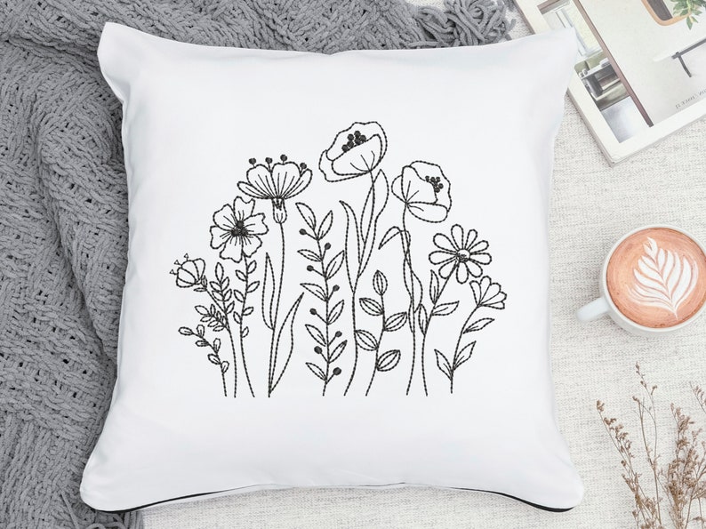 Op de afbeelding: Een wit kussen met een zwart geborduurd bloemenmotief met verschillende bloemen en bladeren.