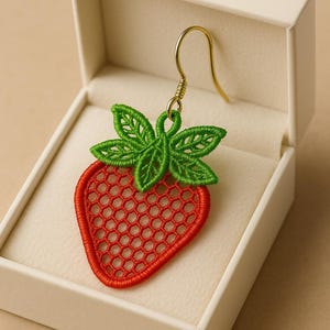 Peut inclure: Boucle d'oreille unique en forme de fraise, faite de fil rouge et vert, présentée dans une boîte blanche. La boucle d'oreille présente un motif ajouré détaillé avec un crochet doré. La fraise a un corps rouge et des feuilles vertes.