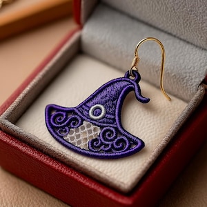 Peut inclure: Boucle d'oreille en forme de chapeau de sorcière violet avec un crochet doré. Le chapeau présente une broderie complexe avec des fils blancs et violets, présenté dans un écrin rouge.
