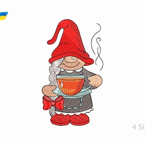 Pode incluir: Desenho bordado de um gnomo com um chapéu vermelho e segurando uma xícara de chá. O gnomo tem barba branca e está vestindo um vestido cinza. O design está disponível em quatro tamanhos.
