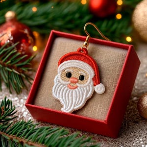 Peut inclure: Boucle d'oreille représentant le Père Noël avec un bonnet rouge et une barbe blanche, présentée dans un coffret rouge. La boucle d'oreille a un crochet doré et est placée sur un fond festif avec des décorations de Noël et de la verdure.