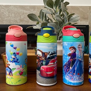May include: Five colorful stainless steel water bottles with different Disney character designs. The bottles have green, blue, and red lids with a push button to open. The bottles are labeled with the names "Efrain", "Eliza", and "Cars".