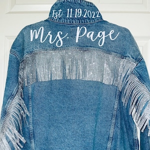 May include: A blue denim jacket with silver fringe and the text "Est. 11.19.2022" and "Mrs. Page" on the back.