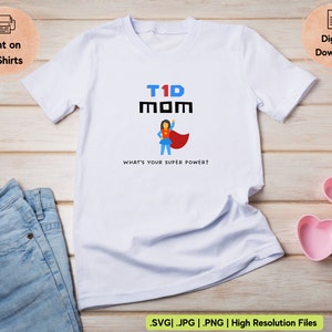 Puede incluir: Camiseta blanca con un gr&aacute;fico negro que dice "T1D MOM" y presenta una mujer superh&eacute;roe de dibujos animados. El texto debajo del gr&aacute;fico dice "&iquest;Cu&aacute;l es tu superpoder?"