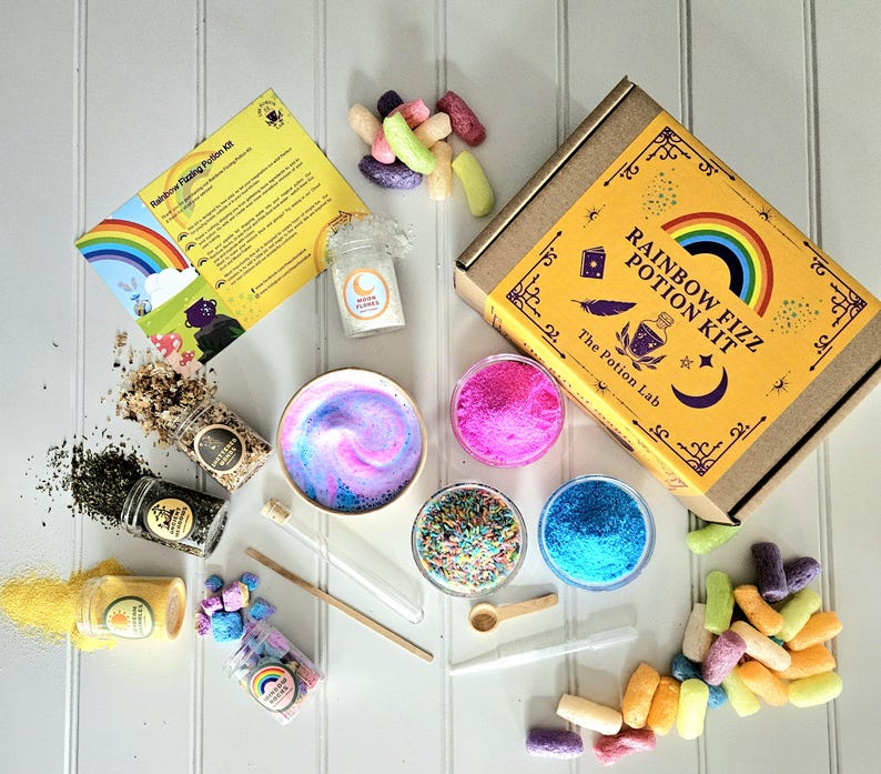 May include: A rainbow fizz potion kit with a yellow box that says "Rainbow Fizz Potion Kit" and "The Potion Lab". The kit includes a variety of ingredients, including colorful sprinkles, powders, and a small bottle of moonflower.