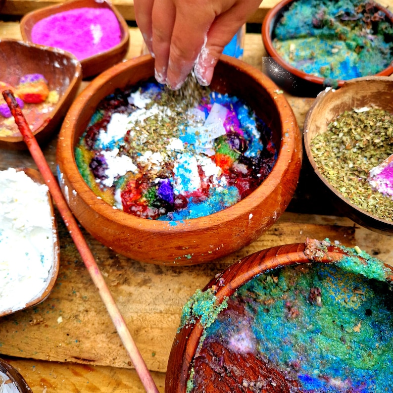 May include: A wooden bowl filled with colorful ingredients, including blue, green, red, and white. A hand is sprinkling a white powder over the mixture.