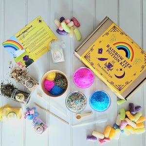 May include: A rainbow fizz potion kit with a yellow box featuring a rainbow and the text "Rainbow Fizz Potion Kit" and "The Potion Lab". The kit includes ingredients in small jars, colorful sprinkles, and other supplies for making fizzy potions.