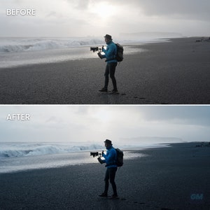 May include: A person wearing a blue jacket and a hat is standing on a black sand beach, holding a camera with a stabilizer. The person is looking at the camera and the background is a cloudy sky and a large wave.