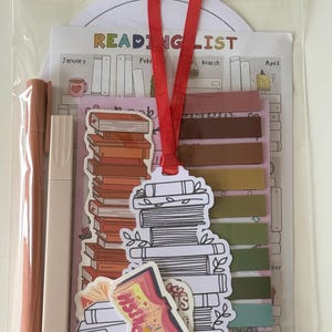 Puede incluir: Un conjunto de lectura en un paquete de plástico transparente. Incluye una lista de lectura, pegatinas, notas adhesivas y dos rotuladores. La lista de lectura muestra el texto «READING LIST». Las pegatinas y el marcapáginas tienen diseños de libros.