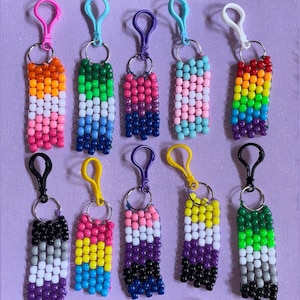 May include: Ten rectangular keychains made of small plastic pony beads arranged in various color patterns. Each keychain features a plastic lobster clasp attached to a metal ring, with bead columns displaying distinct horizontal color stripes.