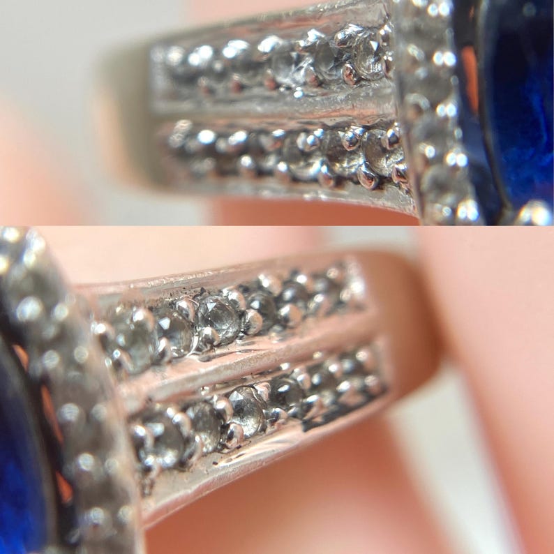 May include: Close-up of a silver ring with a large, oval, deep blue gemstone. The ring's band features two rows of small, clear accent stones. The setting around the blue stone is also adorned with smaller, clear stones, creating a sparkling effect.