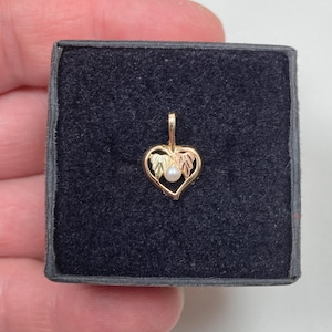 May include: A gold heart-shaped pendant featuring a small white pearl at the center and two textured leaf accents on the sides. The pendant has a small bail at the top for attachment to a chain, showcasing a combination of yellow and rose gold tones.