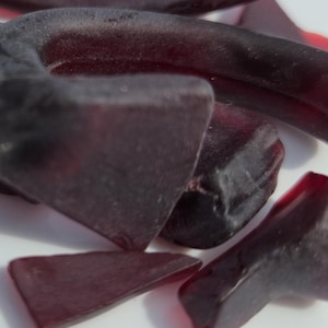 Peut inclure: Gros plan de plusieurs morceaux de verre de mer rouge foncé. Les formes varient, certaines apparaissant triangulaires et d'autres plus arrondies. Le verre a un aspect lisse et givré, suggérant qu'il a été poli par l'océan.