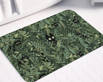 Peut inclure: Un tapis de bain rectangulaire avec un motif de feuillage vert et des visages de chats noirs cachés. Le tapis est placé devant une baignoire blanche. Le texte "CHARMEDVILLE" est visible.