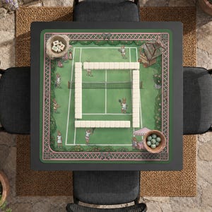 Pode incluir: Um tapete de jogo quadrado com uma ilustração de um campo de ténis com coelhos a jogar, rodeado por uma borda rosa e verde. No centro, existe uma disposição retangular de peças de mahjong brancas, com uma pequena taça de dados e berlindes.