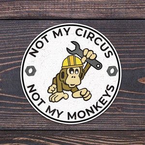 May include: A white circle sticker with the text "Not My Circus, Not My Monkeys" in black. A cartoon monkey wearing a yellow hard hat holds a wrench.