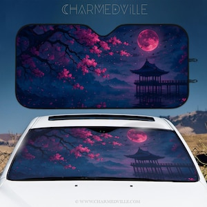 May include: Car sunshade featuring a Japanese-inspired landscape with a full pink moon, cherry blossoms, and a pagoda reflected in the water. The text "CHARMEDVILLE" is at the top. The sunshade is displayed on a white car.