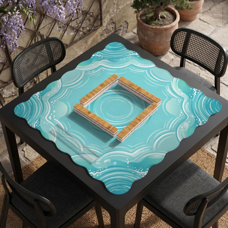 May include: A square, black table with a blue placemat featuring a water wave design. A square wooden frame sits on the placemat. Two black chairs are on either side of the table. The table is on a woven mat.