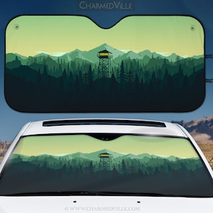 May include: A green and yellow car sunshade with a silhouette of a forest and a lookout tower. The text "CHARMEDVILLE" is at the top of the sunshade. The text "WWW.CHARMEDVILLE.COM" is at the bottom of the sunshade.