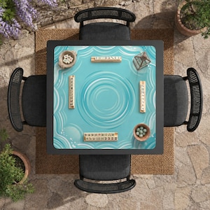 May include: Overhead view of a square black table with a light blue surface featuring a water ripple design. The table is surrounded by four black chairs. Mahjong tiles and small bowls are placed on the table, suggesting a game setup.