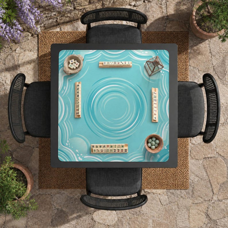 May include: Overhead view of a square black table with a light blue surface featuring a water ripple design. The table is surrounded by four black chairs. Mahjong tiles and small bowls are placed on the table, suggesting a game setup.