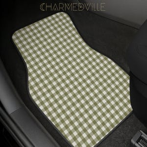 May include: A car floor mat featuring a sage green and white gingham check pattern. The mat has a black border and is positioned in a vehicle footwell. The text CHARMEDVILLE is visible at the top center of the image in a thin, gold font.