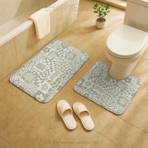 Könnte beinhalten: Ein Badezimmer-Set mit einer rechteckigen Badematte und einer U-förmigen Toilettenmatte, beide mit einem hellgrünen und weißen Muster. Zwei Paar weiße Hausschuhe liegen auf dem Boden. Eine Toilette, eine Badewanne und eine kleine Pflanze sind ebenfalls zu sehen.